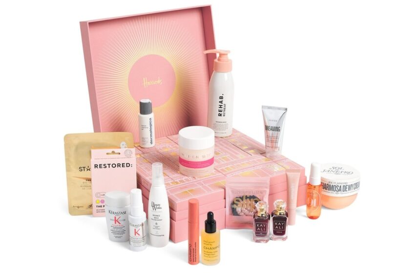 The Harrods 12 Days of Hair & Body Advent Calendar 2026 open, with its 18 haircare, body and fragrance products in front of the pink calendar