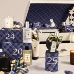 The Jo Malone Christmas Kist Advent Calendar 2026 trunk open among numbered crackers and tartan stockings, with colognes, body care and travel candles around it