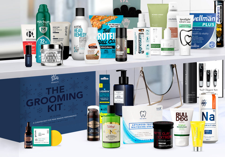 The 30 products from the Latest in Beauty Grooming Kit advent calendar arranged on bathroom shelves above the navy box