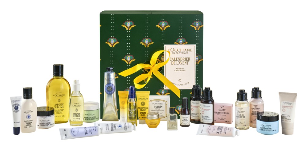 The closed L'Occitane Prestige Advent Calendar box, dark green with a yellow ribbon, with its products arranged around it