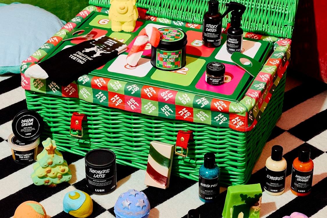 The open Lush Advent Calendar 2026 hamper on a striped rug, its tray full of festive products with more bath bombs and bottles in front