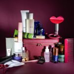 The burgundy Niche Beauty case with all the calendar products arranged around it, including a red lip-shaped hair clip, a cherry red comb, serums, creams and a candle