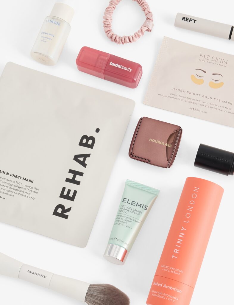 A flat lay of Selfridges Dream Bundle 2026 products, including the REHAB. Collagen Sheet Masks, Elemis Pro-Collagen Marine Cream SPF30, a Hourglass Ambient powder compact and a Slip silk scrunchie