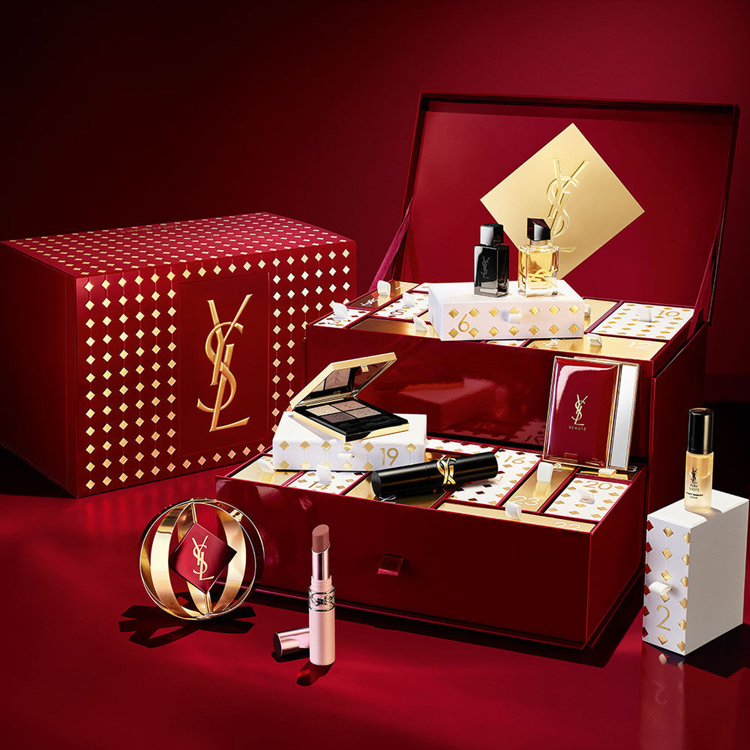 The burgundy YSL advent calendar with its drawers pulled out, fragrances and a Couture Mini Clutch palette set out on a deep red backdrop